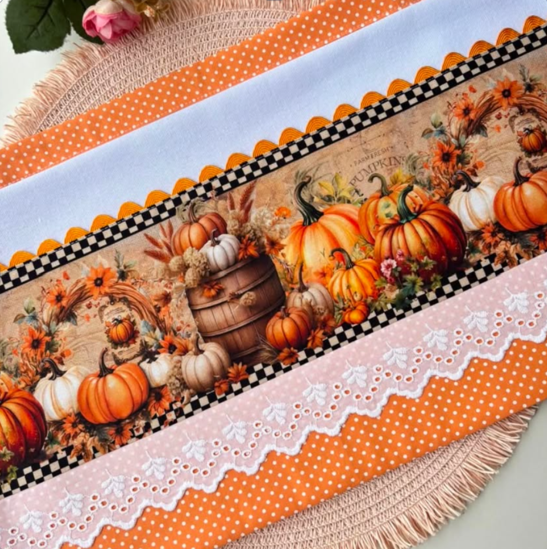 White pumpkin harvest tea towel with wooden barrel and floral wreath print, black-and-white checks, orange polka-dot borders, and white eyelet lace.
