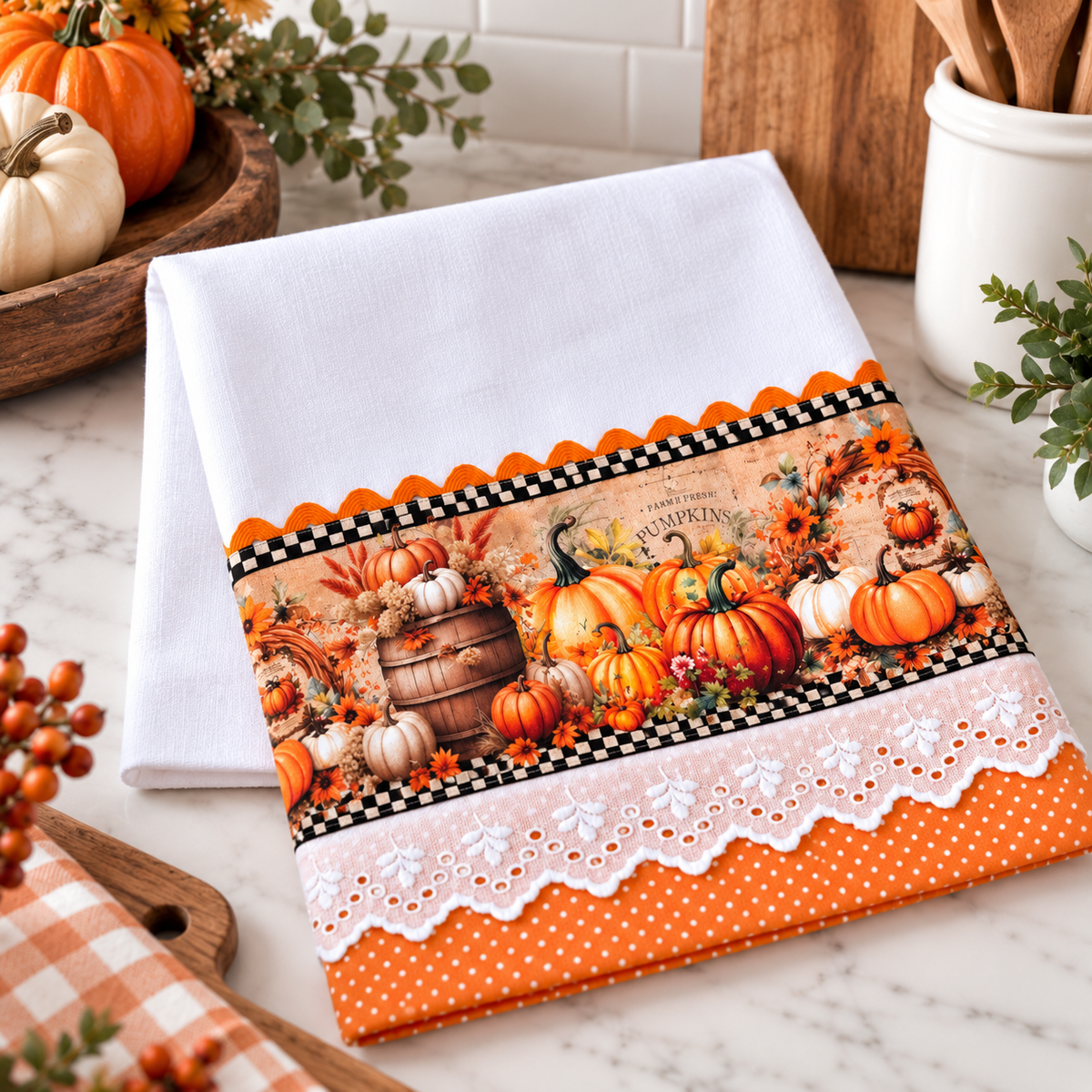 Wooden barrel, pumpkin, and floral tea towel with black-and-white checkerboard trim, white eyelet lace, and orange polka dots on a kitchen counter.