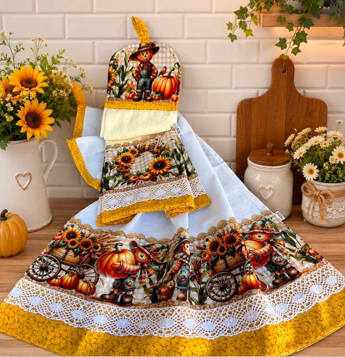 Fall harvest kitchen towel set with a white tea towel and ivory hanging towel featuring scarecrows, pumpkins, sunflowers, and gold trim