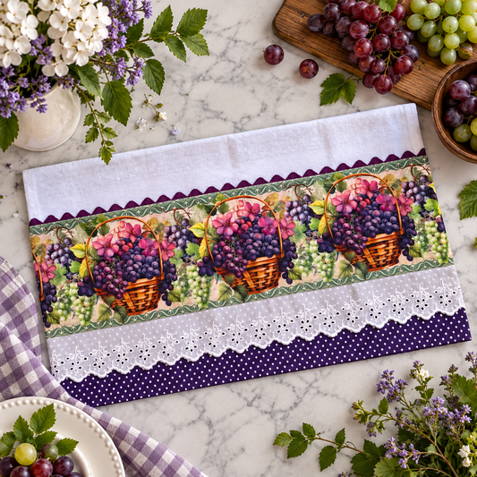 Tuscan Grape Harvest kitchen tea towel 20x30 flat lay on marble surface showing repeating wicker basket print panel overflowing with purple and green grapes and pink blossoms, deep purple polka dot trim with white eyelet lace border, surrounded by fresh purple and green grapes on wooden board lavender flowers in white vase and purple gingham cloth