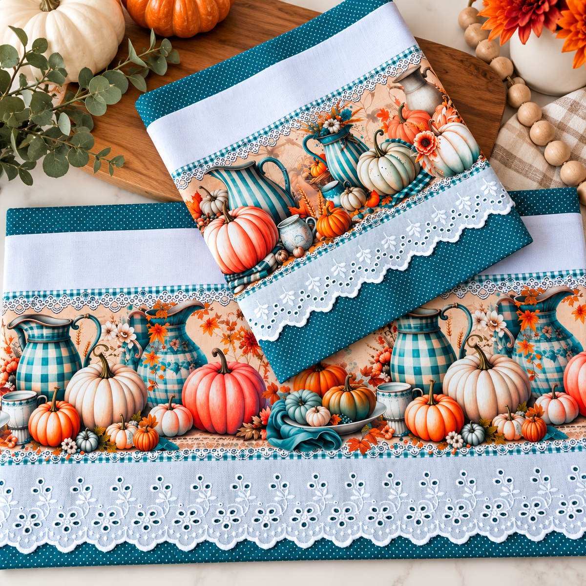 Pumpkin and teal pitcher tea towel set with teal polka dot borders and white eyelet lace, styled with pumpkins, greenery, and orange flowers.