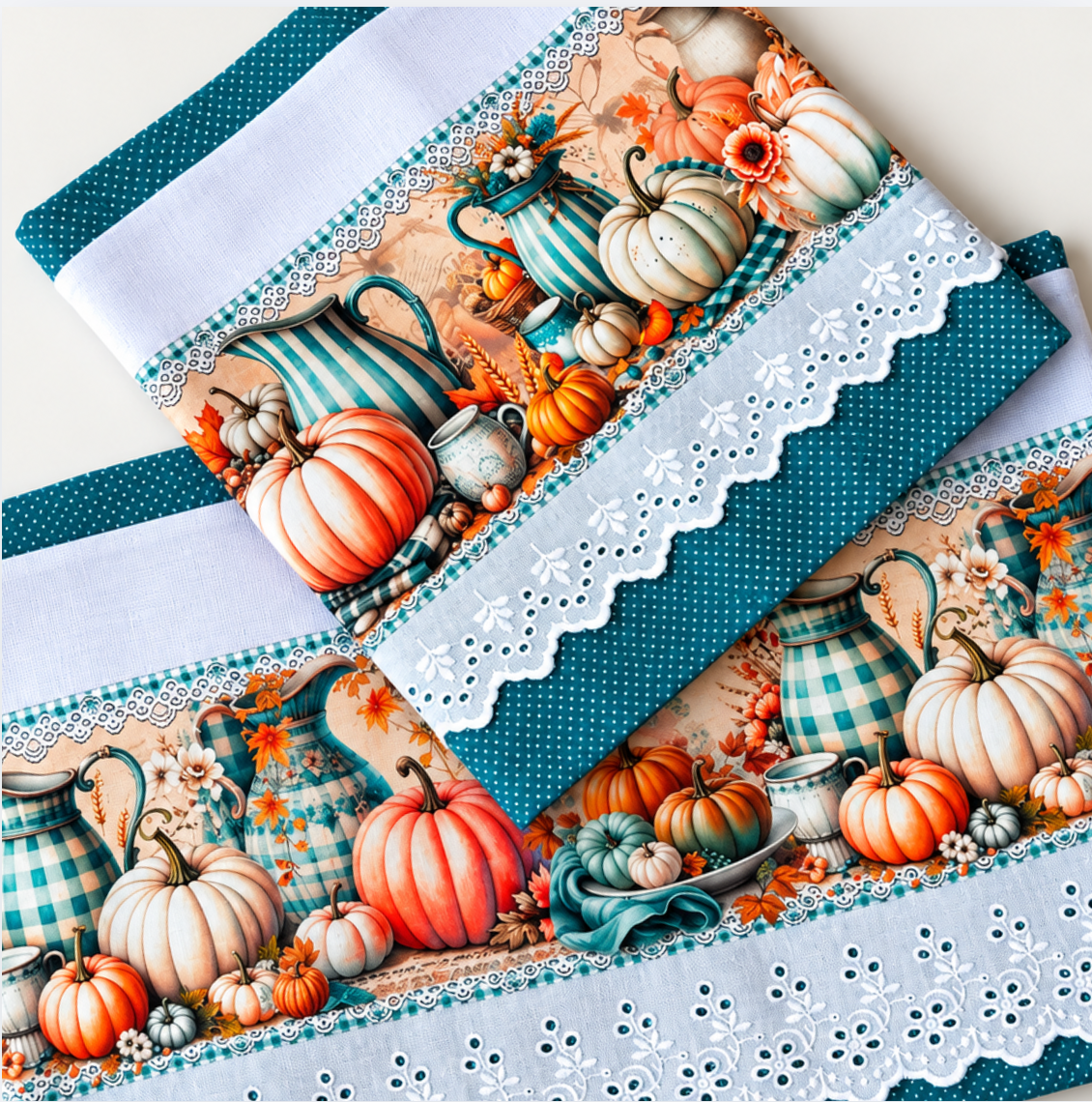 Close-up of pumpkin and teal pitcher prints on two white tea towels with scalloped white eyelet lace and teal polka dot borders.